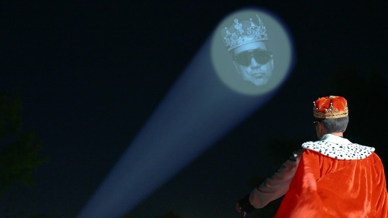 guy in a cape looking at a light signal in the sky