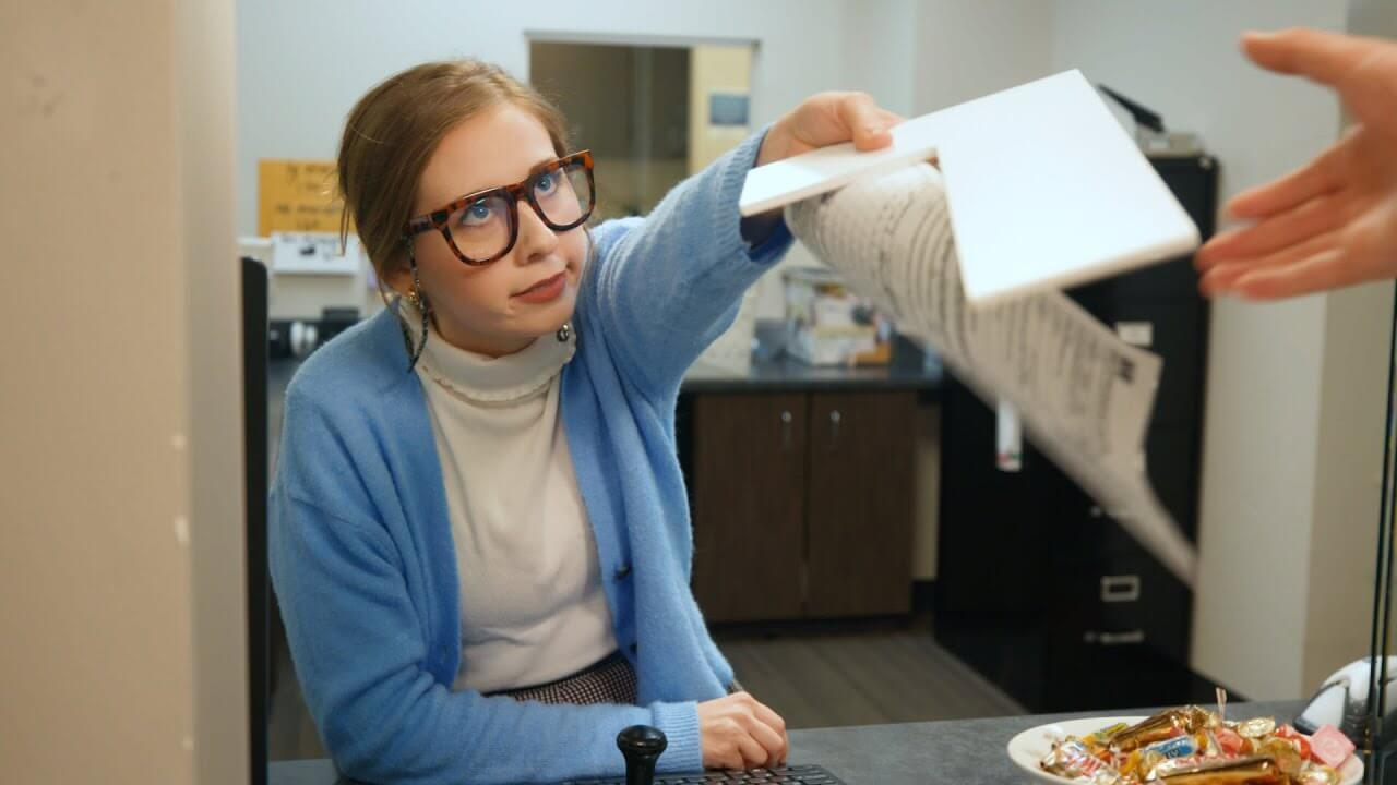 Woman in glasses handing out the letter L
