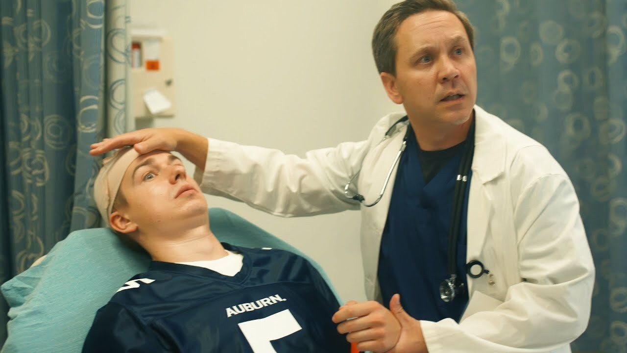 Doctor in white coat checks temperature of college football athlete