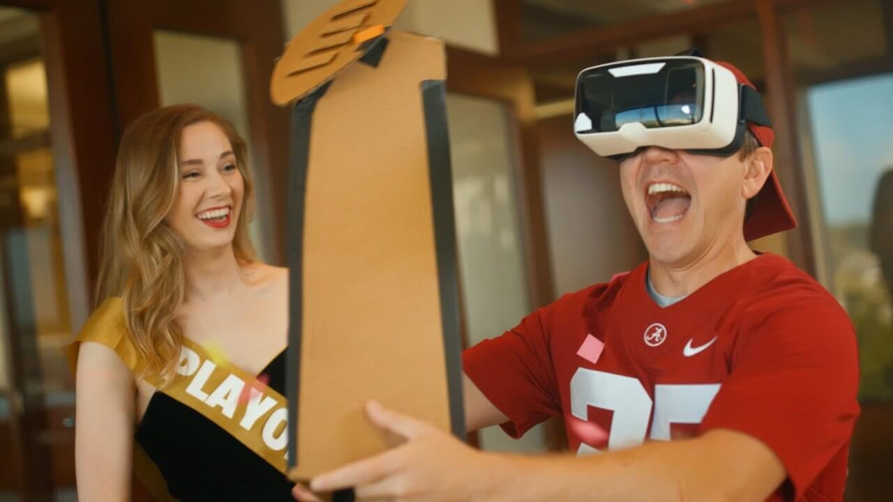 Alabama stands with virtual reality glasses next to the playoff holding a trophy