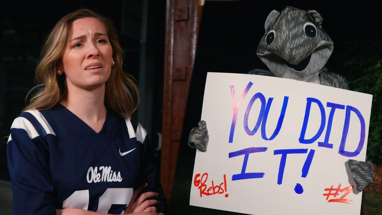girl in an ole miss jersey with someone holding a sign saying "you did it"