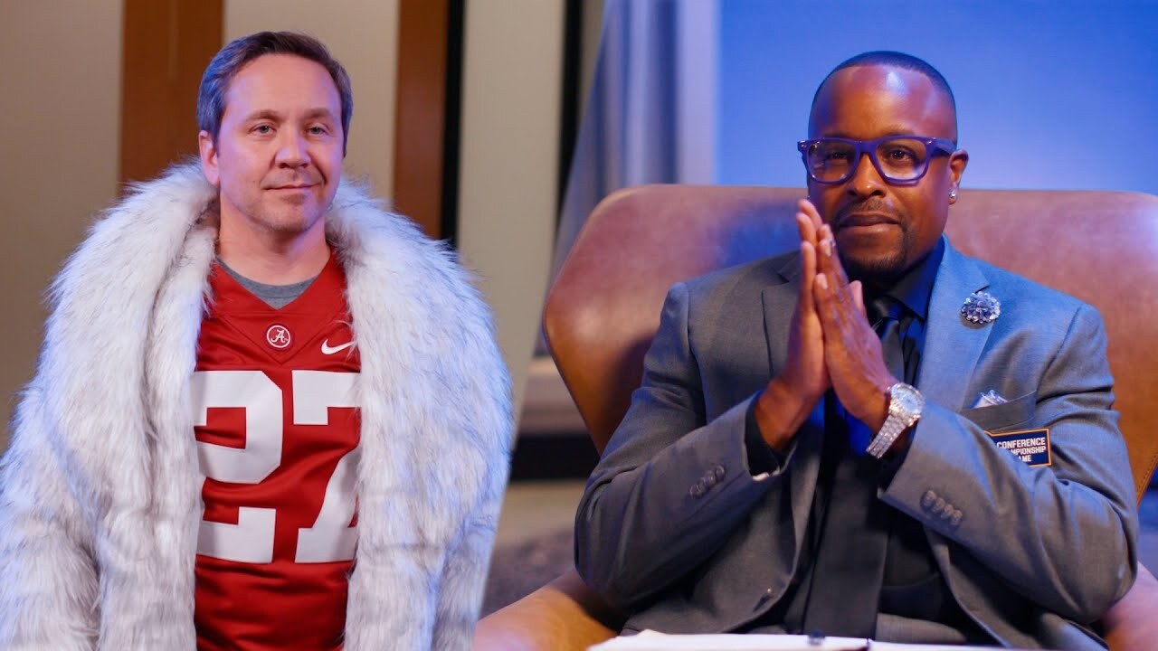Guy in an Alabama jersey wearing a large fuzzy coat and a guy in a suit
