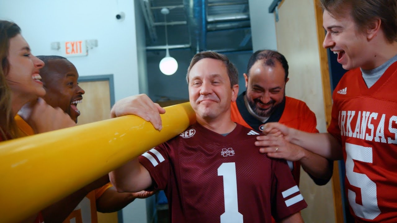 Mississippi State Fan holds part of a goal post while other SEC fans cheer him on