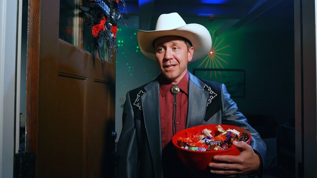 A guy holding bowl of candy dressed as a cowboy